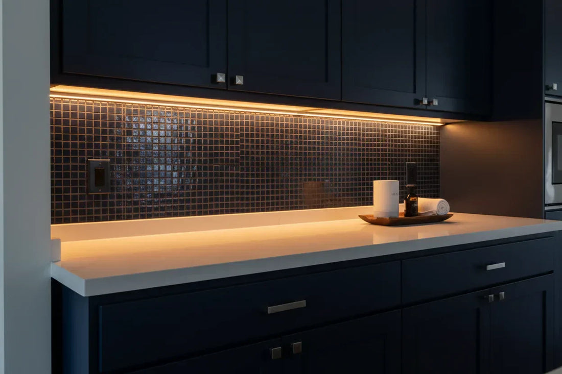 Warm amber LED strip lights installed under dark kitchen cabinets, illuminating a modern countertop