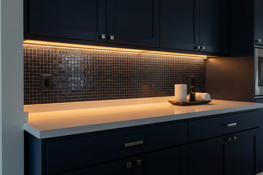 Warm amber LED strip lights installed under dark kitchen cabinets, illuminating a modern countertop