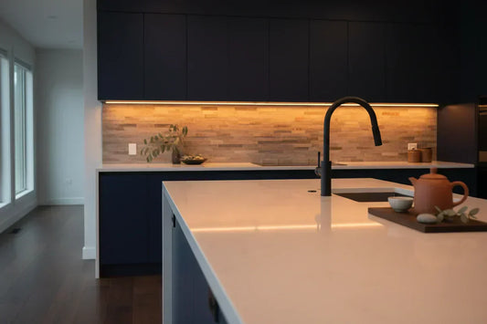 Warm amber LED strip lights installed under dark kitchen cabinets, illuminating a modern countertop
