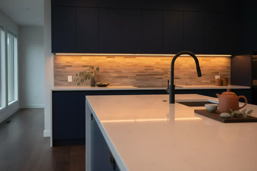 Warm amber LED strip lights installed under dark kitchen cabinets, illuminating a modern countertop